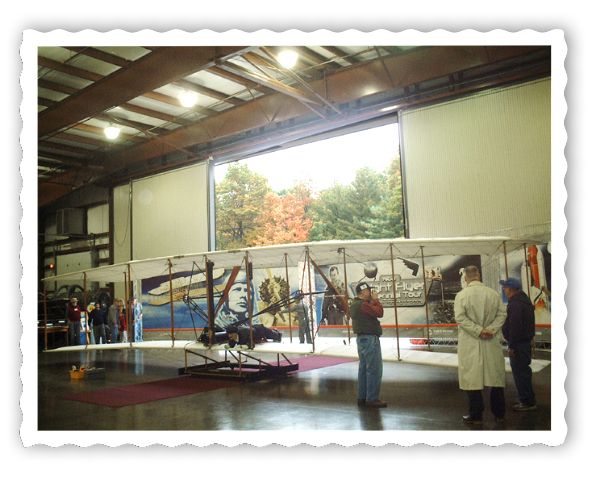 Wright Flyer, hangar door open, beautiful trees as backdrop